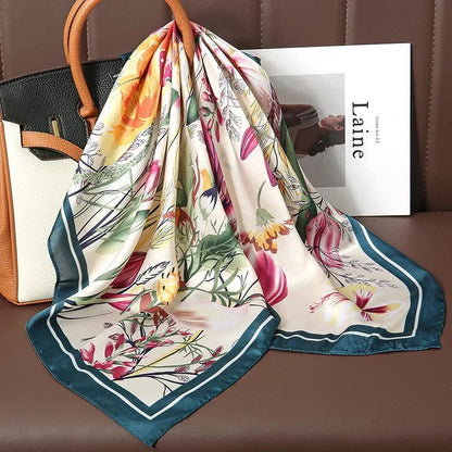 Floral silk scarf with green border draped over a handbag on a brown seat