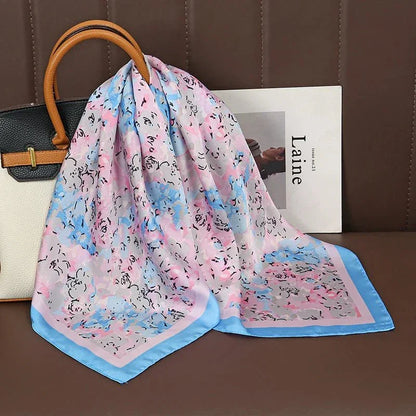 Pastel floral silk scarf with blue border draped on a white handbag on a brown couch