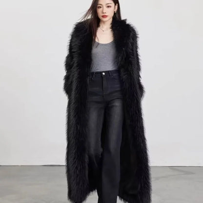 Woman wearing long black faux fur winter coat over gray tank top and black jeans against a plain background