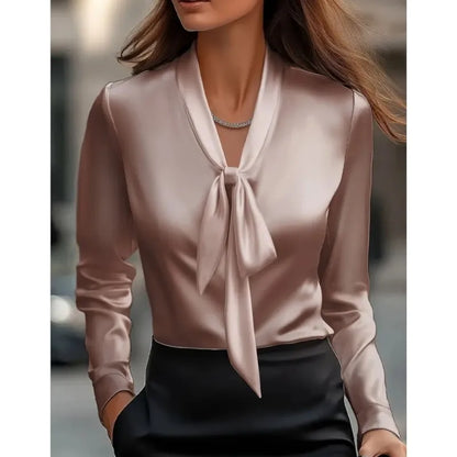 Woman wearing elegant blush satin bow blouse paired with black high-waisted pants in urban setting