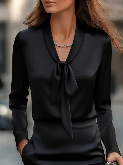 Elegant black satin blouse with bow tie detail, long sleeves, and a silver necklace on model