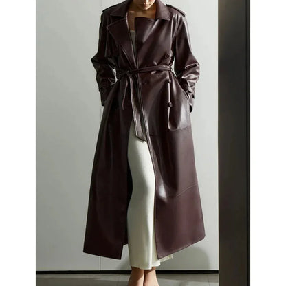 Front view of a long dark brown faux leather trench coat with a belt, worn over a white dress
