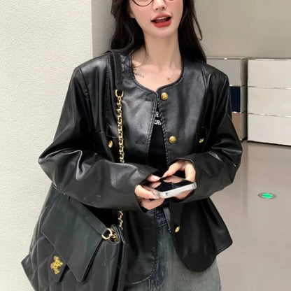 Woman wearing trendy black leather jacket with gold buttons and matching black leather handbag, holding smartphone