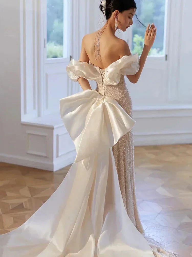 Back view of woman in luxury pearl and sequin evening gown with off-shoulder puff sleeves and large satin bow