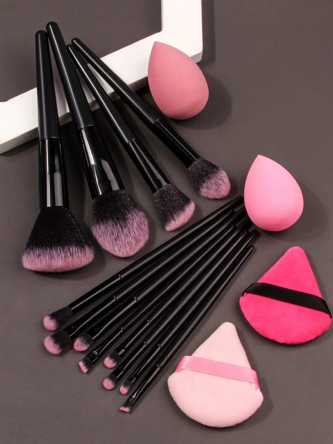Luxury soft makeup brush set with pink and black brushes, sponges, and powder puffs on grey background