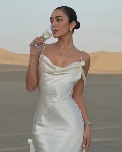 Woman in luxury white satin maxi dress sipping wine in desert setting, elegant style and accessories