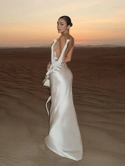 Woman in luxury white satin maxi dress standing on desert sand at sunset