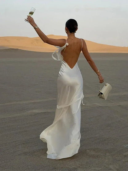 Woman in luxury white satin maxi dress holding a glass and purse in desert landscape