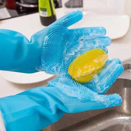 Blue silicone scrubbing gloves with soap foam holding yellow bar soap over kitchen sink