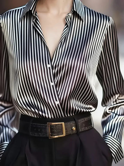 Close-up of a satin striped silk blouse with black and white vertical stripes tucked into black pants with a textured belt