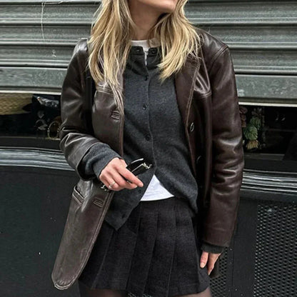 Side view of a woman wearing a brown leather blazer jacket over a dark buttoned sweater and black pleated skirt
