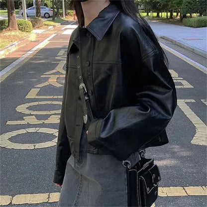 Side view of a woman wearing a black faux leather streetwear shirt jacket and grey skirt outdoors