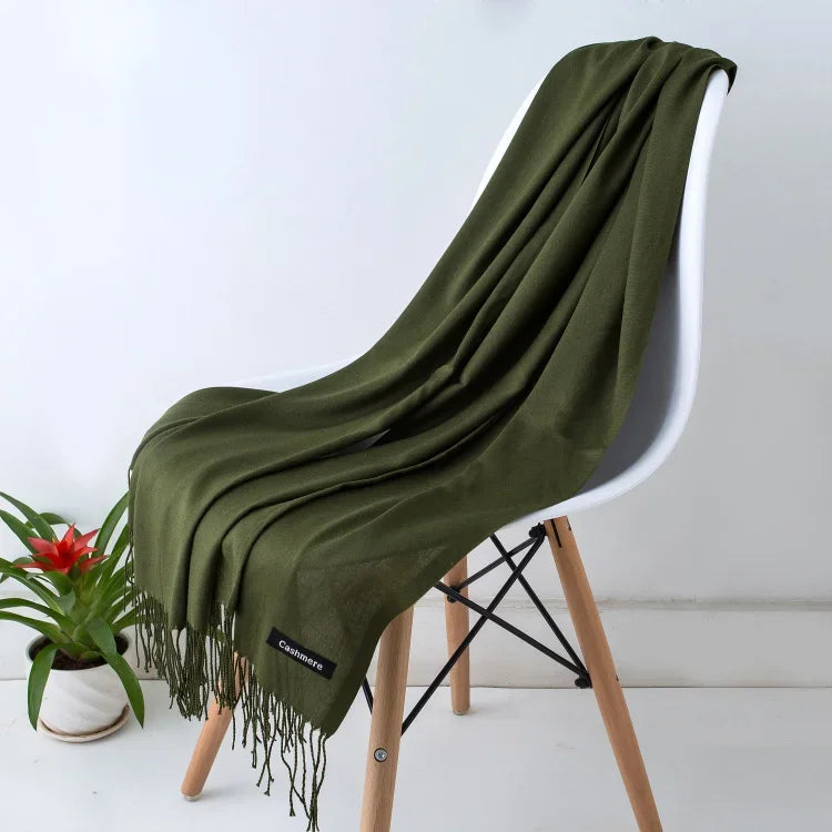 Olive green cashmere scarf with fringe draped over modern white chair, indoor plant nearby