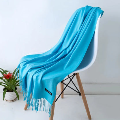 Bright blue cashmere scarf with fringe draped on modern white chair with wooden legs, indoor plant nearby