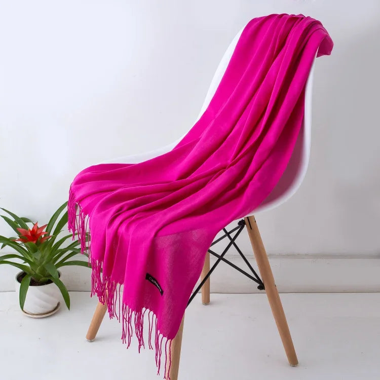 Bright pink women's cashmere scarf with fringes draped over white modern chair, potted plant nearby