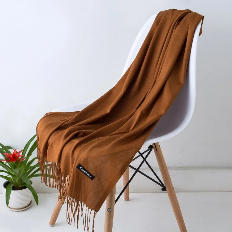 Brown solid color cashmere scarf draped over modern white chair with wooden legs, indoor setting with small potted plant