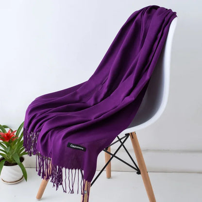 Purple cashmere scarf with fringed edges draped over white modern chair next to small potted plant