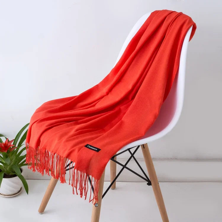 Bright orange solid cashmere scarf with fringe detail draped over modern white chair indoors