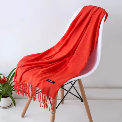 Bright orange solid cashmere scarf with fringe detail draped over modern white chair indoors