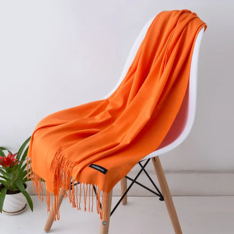 Bright orange cashmere scarf with fringe draped over white modern chair on white floor
