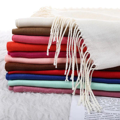 Stack of colorful wool scarves with tassels on a soft fabric background