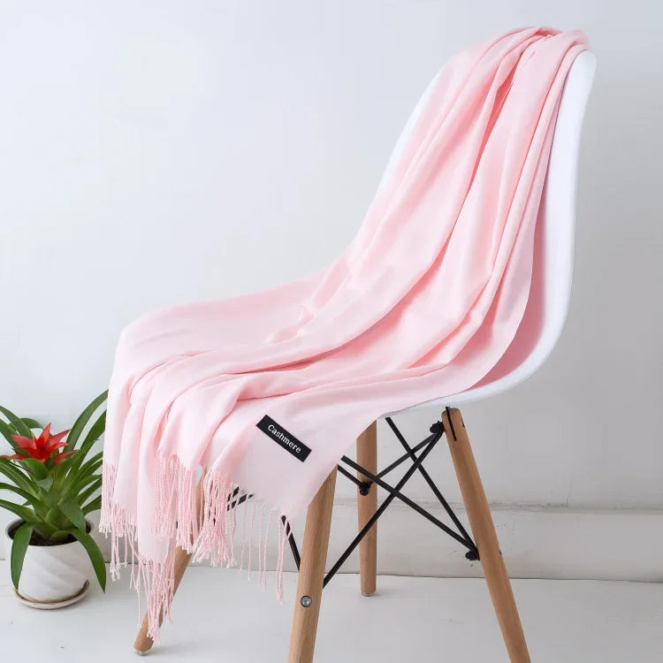 Soft pink cashmere scarf draped over modern white chair with wooden legs, styled beside a green plant