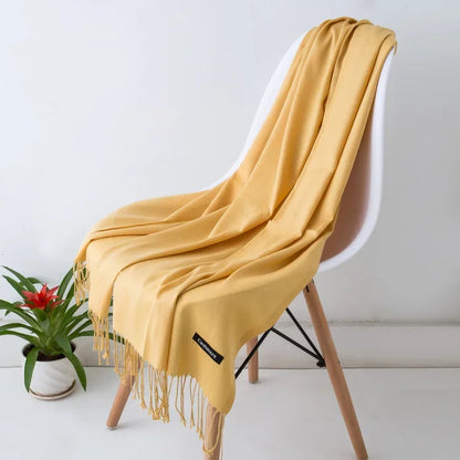 Mustard yellow women's cashmere scarf draped over white modern chair with wooden legs beside green plant