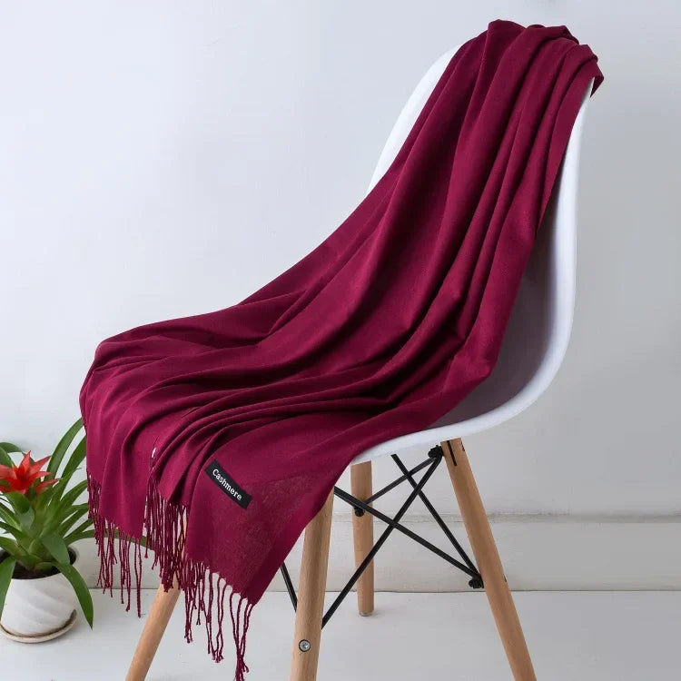 Luxurious solid color women's cashmere scarf in deep burgundy draped over modern white chair with wooden legs, cozy autumn winter shawl