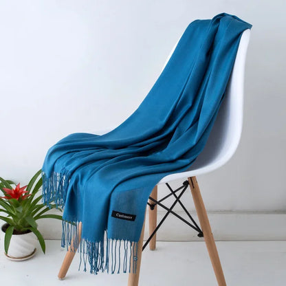 Blue cashmere women's scarf draped over modern white chair with wooden legs, indoor plant nearby