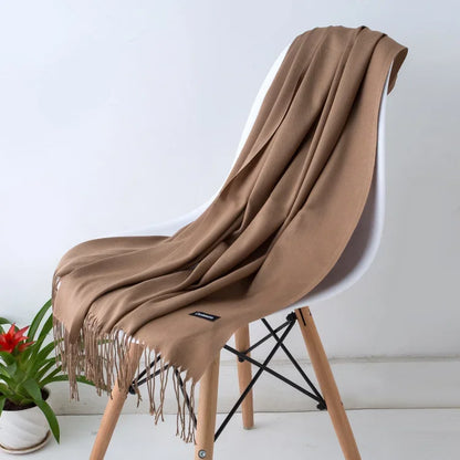 Soft solid color camel cashmere scarf with fringe edges draped over white modern chair with wooden legs