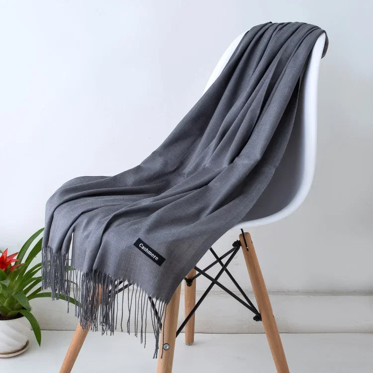 Soft grey cashmere scarf with fringe detail draped over white modern chair in minimalist setting
