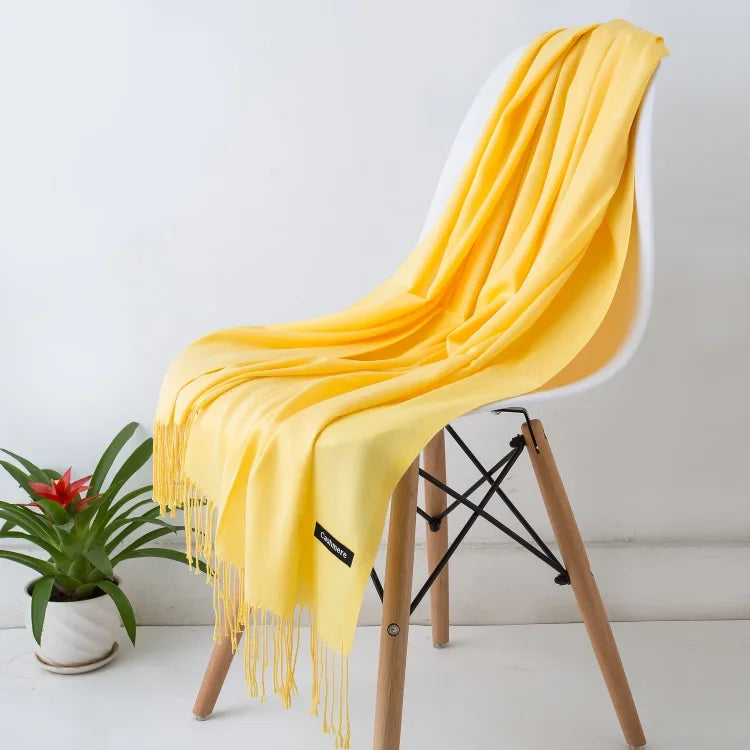 Yellow cashmere scarf with fringe draped over modern white chair with wooden legs, next to green potted plant