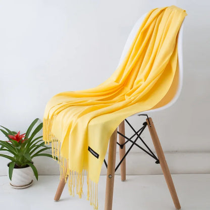 Yellow cashmere scarf with fringe draped over modern white chair with wooden legs, next to green potted plant