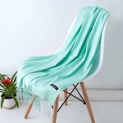 Light blue cashmere scarf draped over modern white chair with wooden legs, next to potted plant