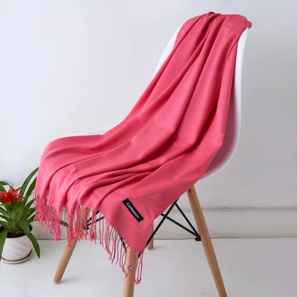 Pink women's cashmere scarf with fringes draped over modern white chair in minimalist setting