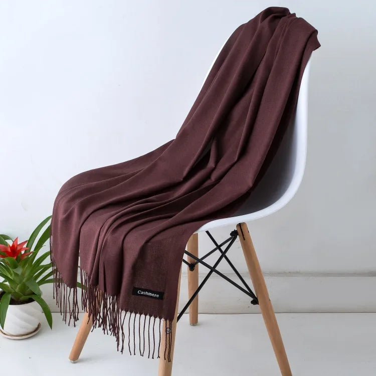 Brown cashmere women's scarf draped over white modern chair with wooden legs, potted plant nearby