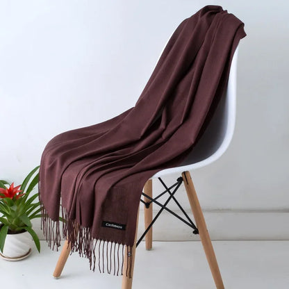 Brown cashmere women's scarf draped over white modern chair with wooden legs, potted plant nearby