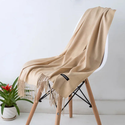 Beige cashmere scarf with fringed edges draped over modern white chair beside potted green plant