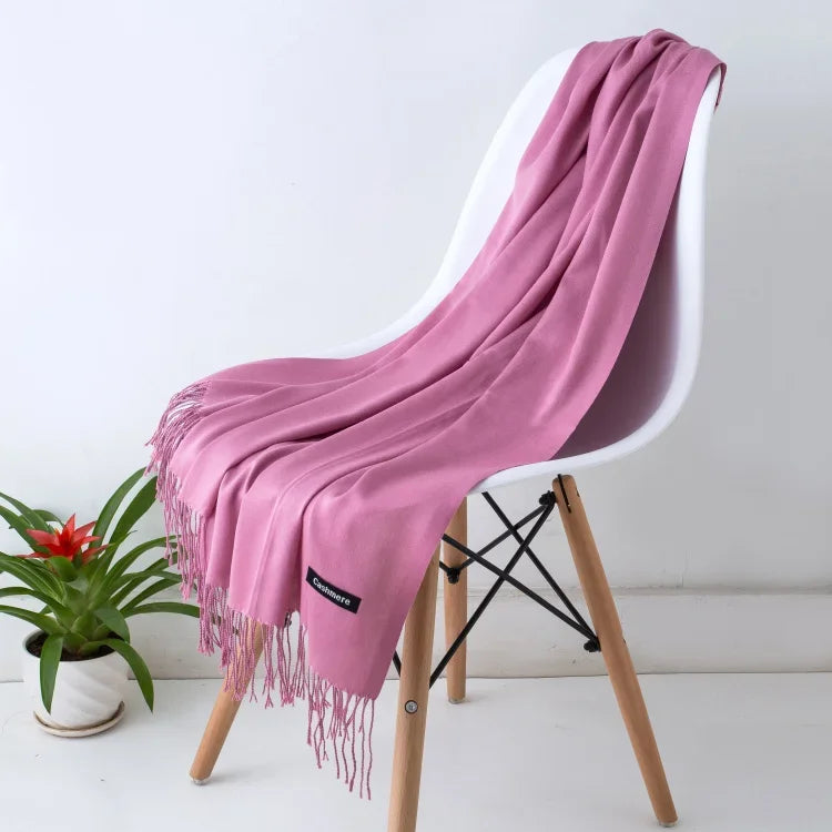 Soft pink cashmere scarf draped over a modern white chair with wooden legs beside a potted green plant