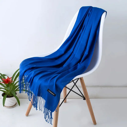 Blue women's cashmere scarf with fringes draped over a modern white chair next to a small potted plant