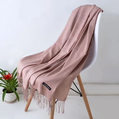 Soft solid color cashmere scarf draped over white chair with wooden legs, green plant nearby