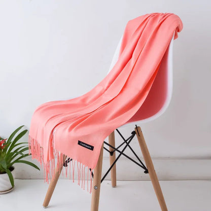 Soft coral pink cashmere scarf draped over modern white chair with wooden legs, minimalist setting