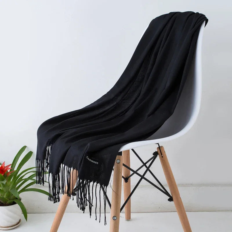 Black cashmere scarf with fringe draped on modern white chair, potted plant beside