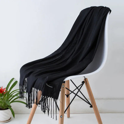 Black cashmere scarf with fringe draped on modern white chair, potted plant beside