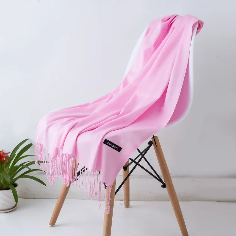 Light pink cashmere shawl with fringe draped over white chair, indoor modern setting