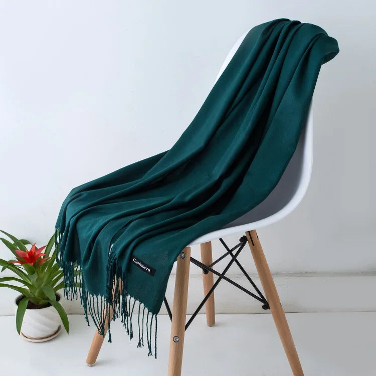 Dark green cashmere scarf with fringes draped over a modern white chair, indoor setting