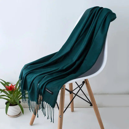 Dark green cashmere scarf with fringes draped over a modern white chair, indoor setting