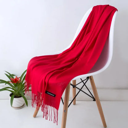 Bright red cashmere scarf with fringes draped on modern white chair, indoor plant nearby