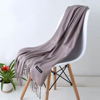 Soft taupe cashmere scarf draped over modern white chair with wooden legs, next to green potted plant