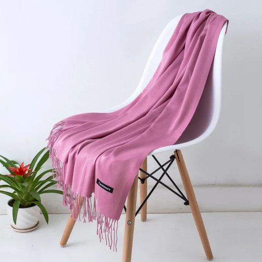 Pink cashmere scarf with fringes draped on white modern chair, indoor setting, potted plant